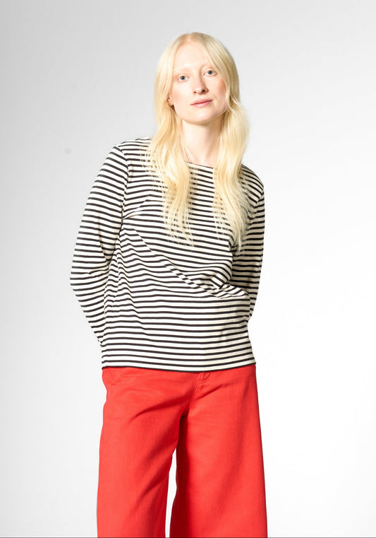A blonde woman modeling a black and white horizontally striped long-sleeve top from Mademoiselle Eye with red wide-leg pants, standing against a light gray studio background.