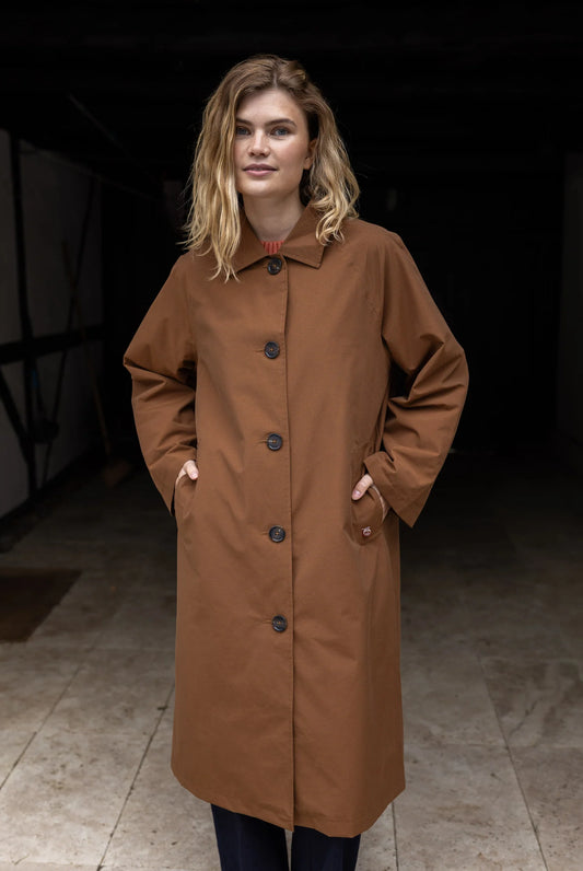 Woman wearing a brown coat standing in a dimly lit room.