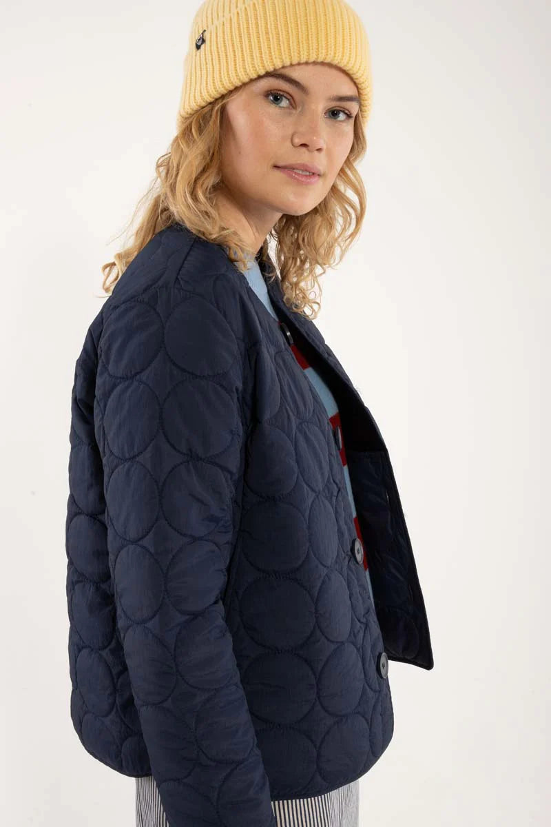 Daneland quilted jacket from Danefae Copenhagen in classic navy. Perfect as a thermo layer underneath a coat or worn by itself as a transitional jacket. Round neck, long sleeves and button closure with four buttons in the same colour as the jacket. Roomy side pockets. Round hem. Made from 100% nylon. Water repellent in light showers.
