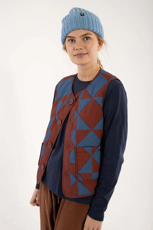 Quilted thermo gilet from Danefae Copenhagen. Regular length, round neck, button closure with four buttons, roomy patch pockets. Featuring a geometric pattern of diametrically placed squares and triangles in brick red and denim blue. Made from nylon.
