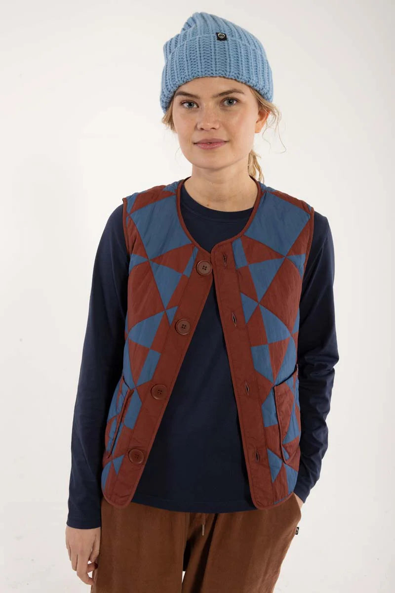 Quilted thermo gilet from Danefae Copenhagen. Regular length, round neck, button closure with four buttons, roomy patch pockets. Featuring a geometric pattern of diametrically placed squares and triangles in brick red and denim blue. Made from nylon.