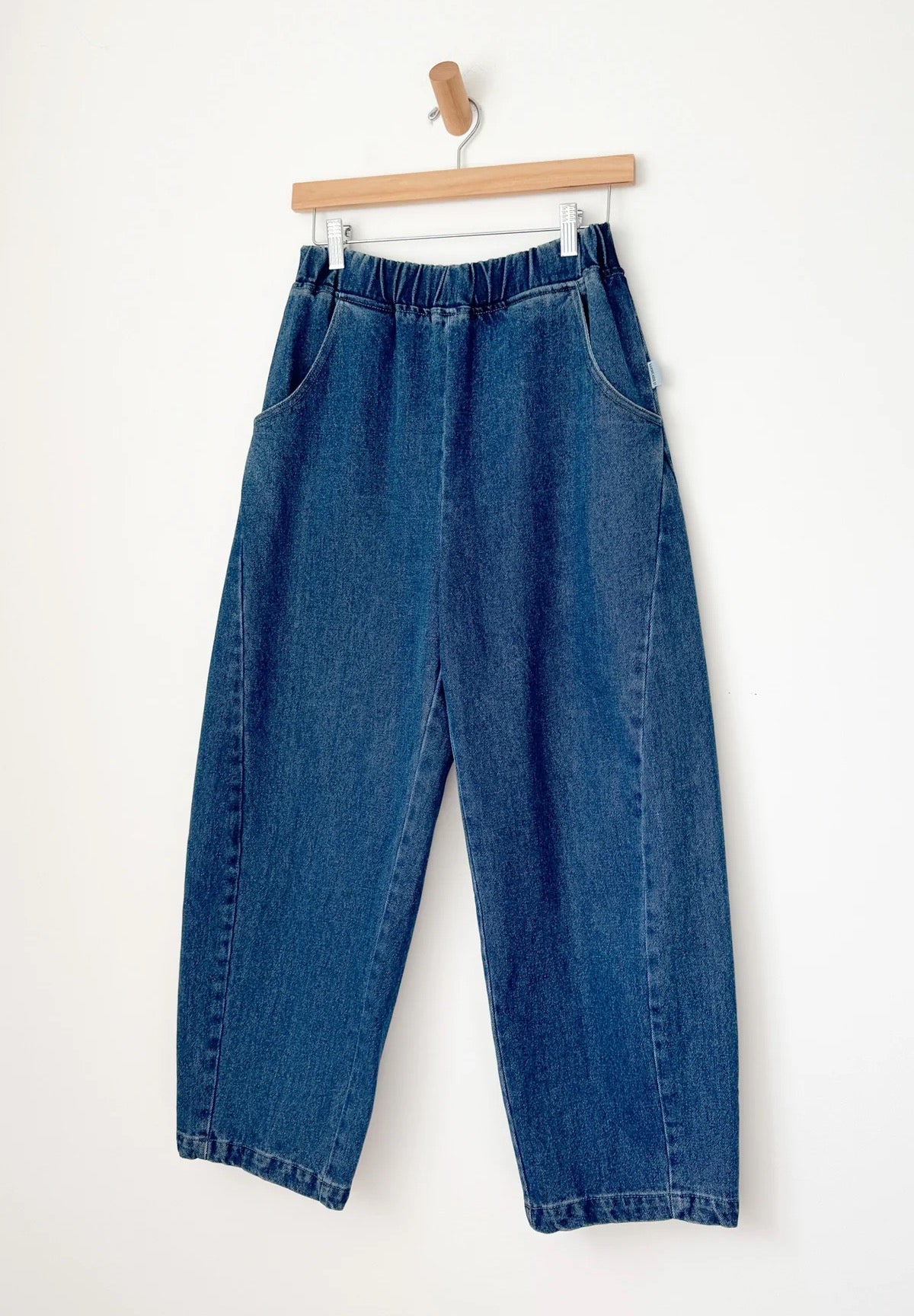 Arc Pants from Le Bon Shoppe. Barrel leg jeans made from durable 100% cotton denim. Featuring an elastic high waist, deep side pockets, and a slightly curved, cropped leg with a unique side panel. In a mid denim blue colour.