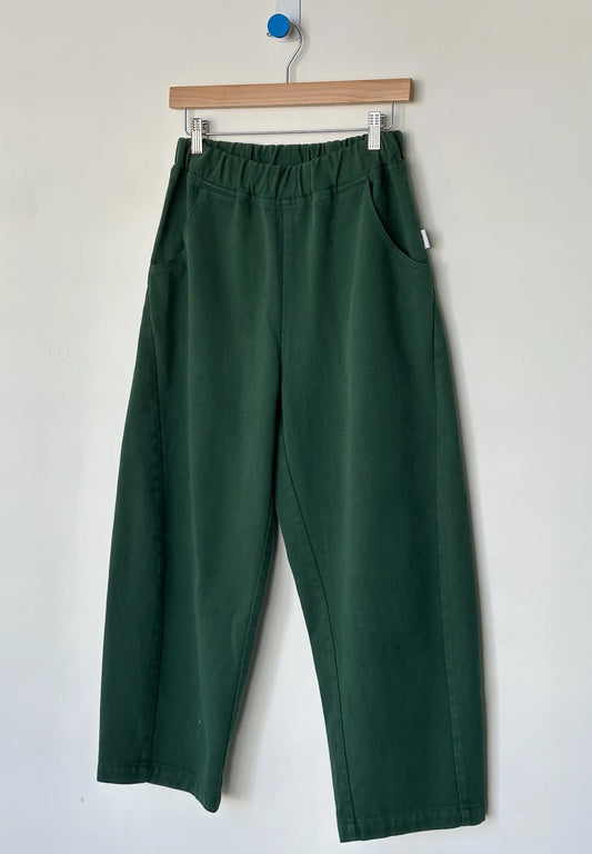 Arc Pants from Le Bon Shoppe. Barrel leg trousers made from durable cotton canvas. Featuring an elastic high waist, deep side pockets, and a slightly curved, cropped leg with a unique side panel. In a deep pine green colour.