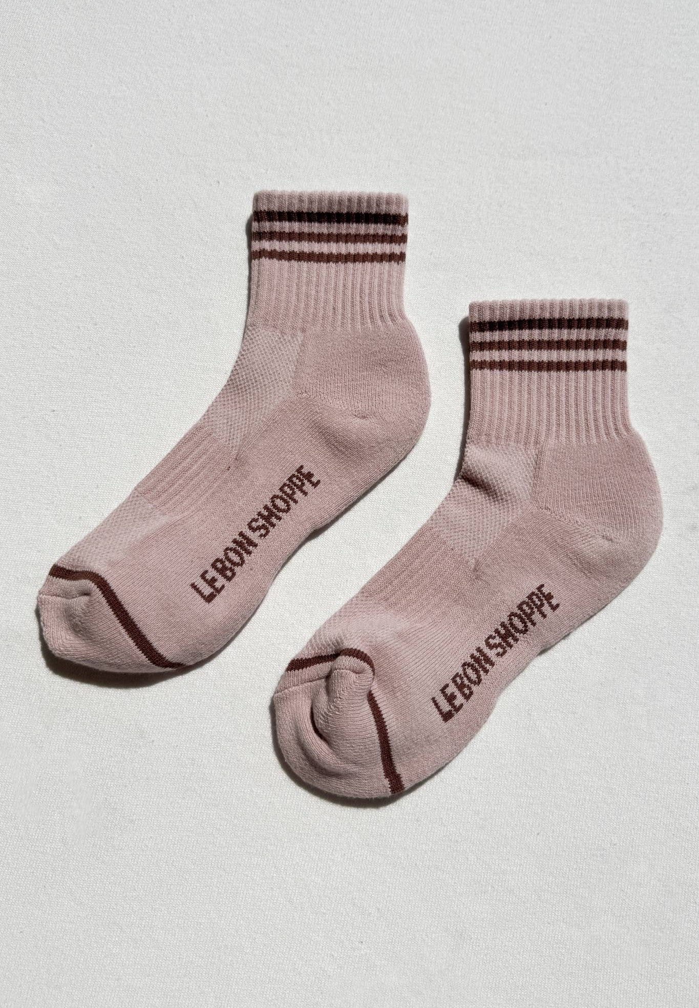 Pair of pink socks with brown stripes and 'Le Bon Shoppe' branding on a light gray background