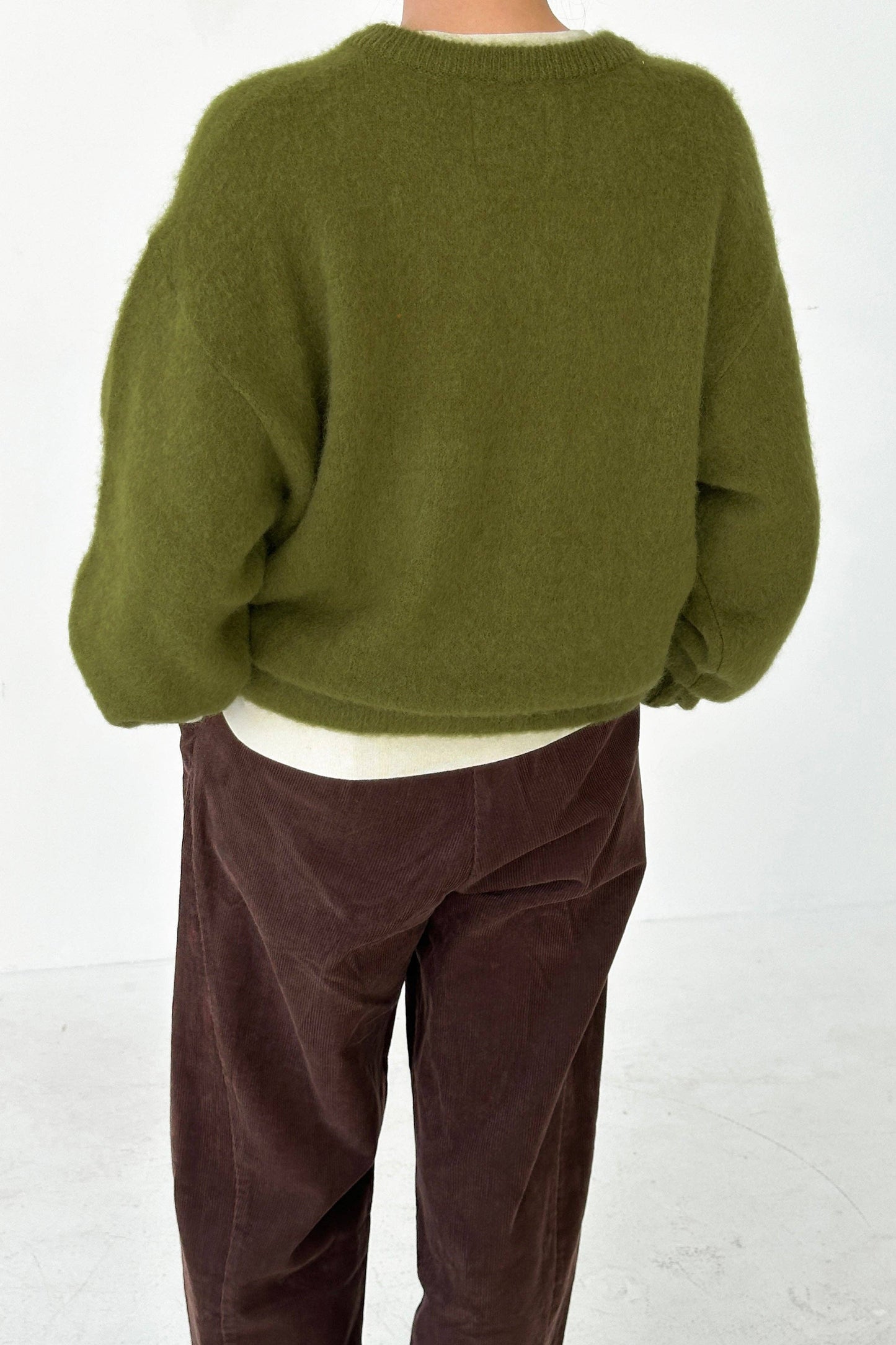 Person wearing a leaf green mohair James sweater from Le Bon Shoppe and brown pants on a white background