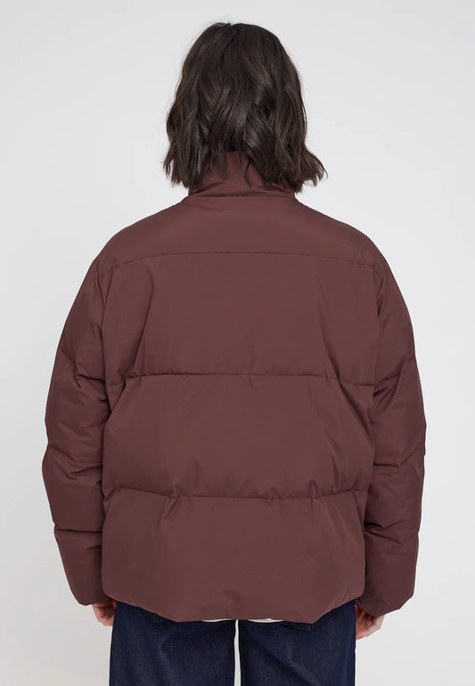 Woman wearing a chocolate brown loose fit puffer jacket on a white background