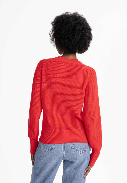 Women’s rib knit jumper by Mela. Made from 100% organic cotton, in a bright hue of poppy red. Crew neck, long, slightly bell-shaped sleeves. Subtle V-shaped pattern on the front. Regular fit.