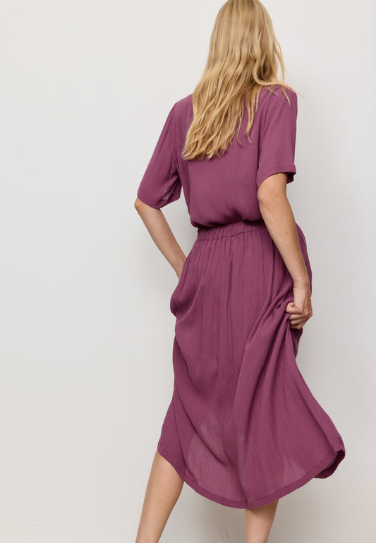 Woman wearing a purple skirt with a matching top against a white background
