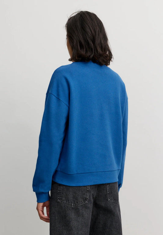 Woman wearing a blue organic cotton sweatshirt from Recolution on a plain background