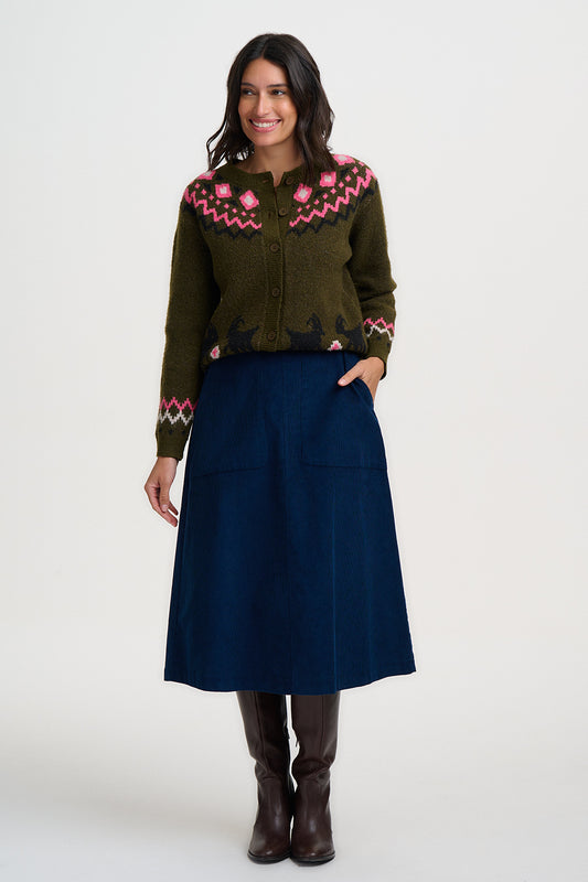 Woman wearing an olive green fair isle cardigan from Sugarhill Brighton with pink floral patterns and a blue skirt on a white background