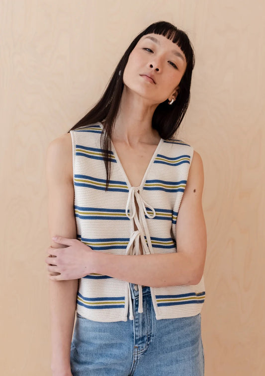 Knitted sleeveless vest from TBCo in cream, with fine horizontal stripes in dark blue and pistachio green. Made from 100% high-quality cotton. With two front ties for adjustable styling.