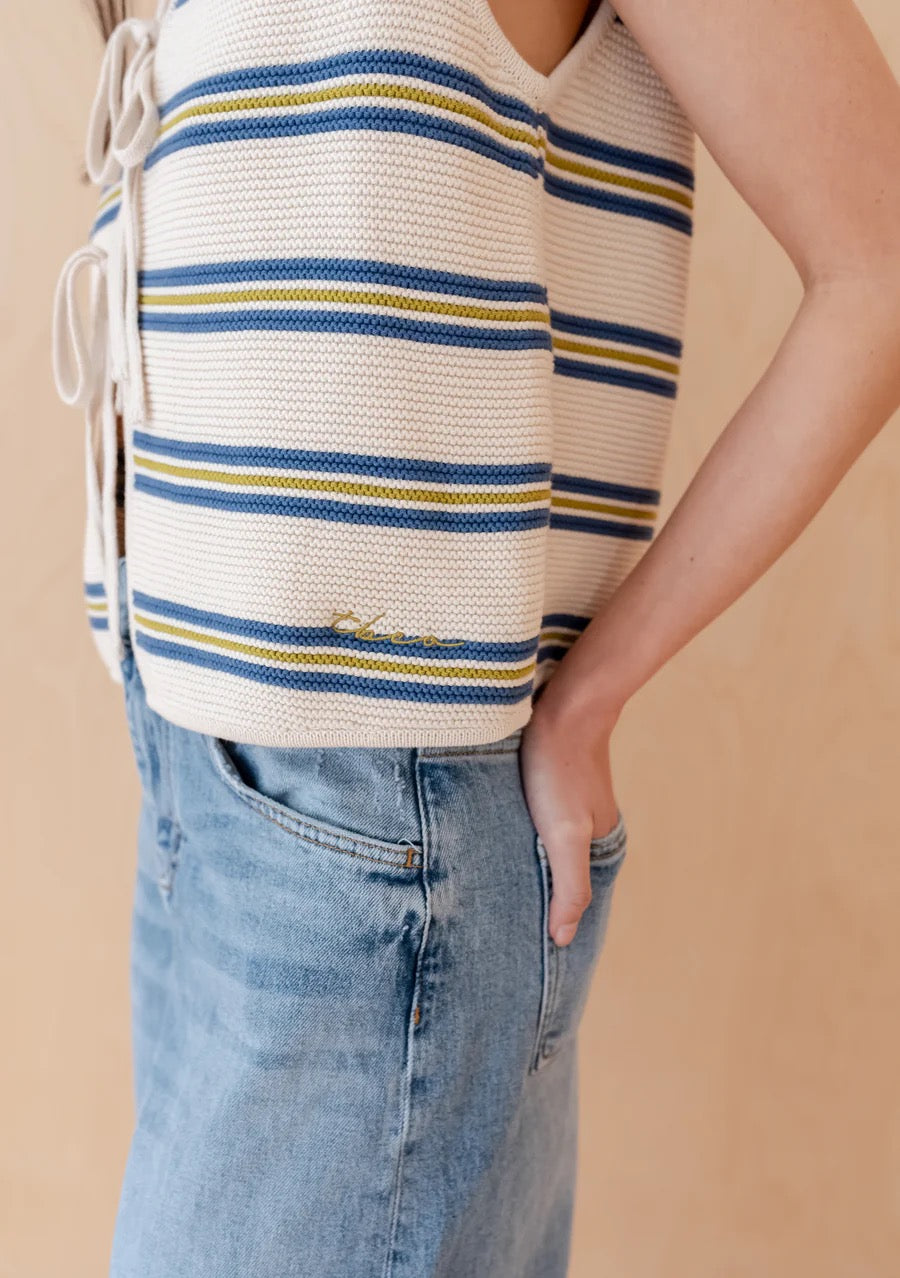 Knitted sleeveless vest from TBCo in cream, with fine horizontal stripes in dark blue and pistachio green. Made from 100% high-quality cotton. With two front ties for adjustable styling.