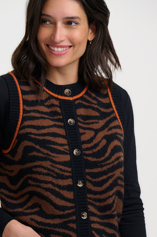 Woman wearing a tiger patterned knitted gilet from Sugarhill Brighton with orange trim on a white background