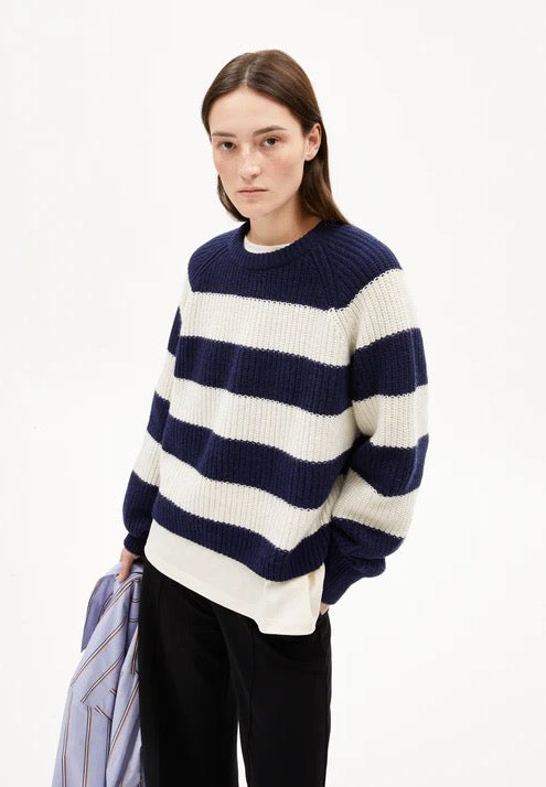 Woman wearing a navy and white striped chunky jumper from Armedangels made from organic wool and organic cotton, on a white background