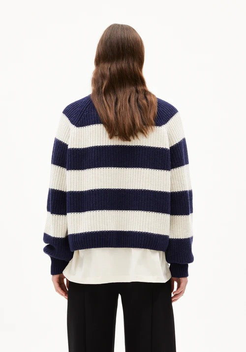Woman wearing a navy and white striped chunky jumper from Armedangels made from organic cotton and organic wool, on a white background