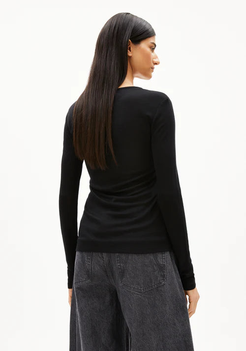 Woman wearing a black long-sleeve wool and Tencel blend top by  Armedangels and gray pants on a white background