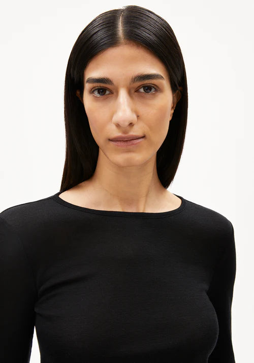 Woman wearing a black long-sleeve wool and Tencel blend top from Armedangels against a white background