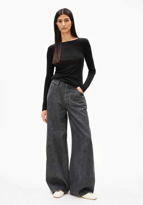 Woman wearing a black long-sleeve wool and Tencel blend top by Armedangels and wide-leg jeans on a white background