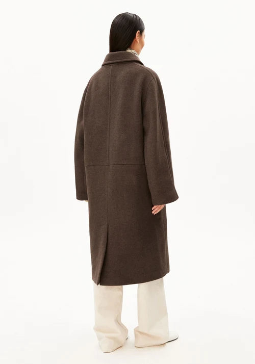 A model shown from the back wearing a dark brown wool-blend coat over cream wide-leg trousers, photographed against a seamless white studio background.