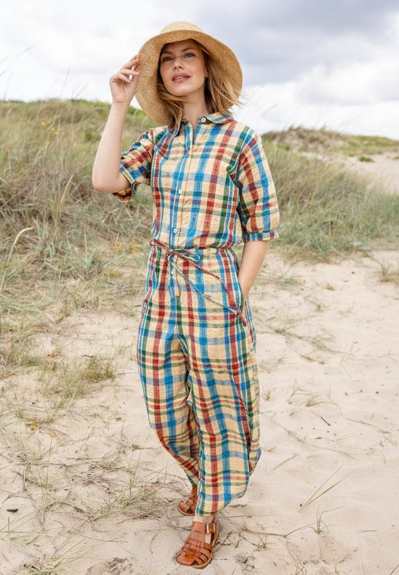 Woman in a plaid jumpsuit standing on sandy dunes with grass and clouds in the background