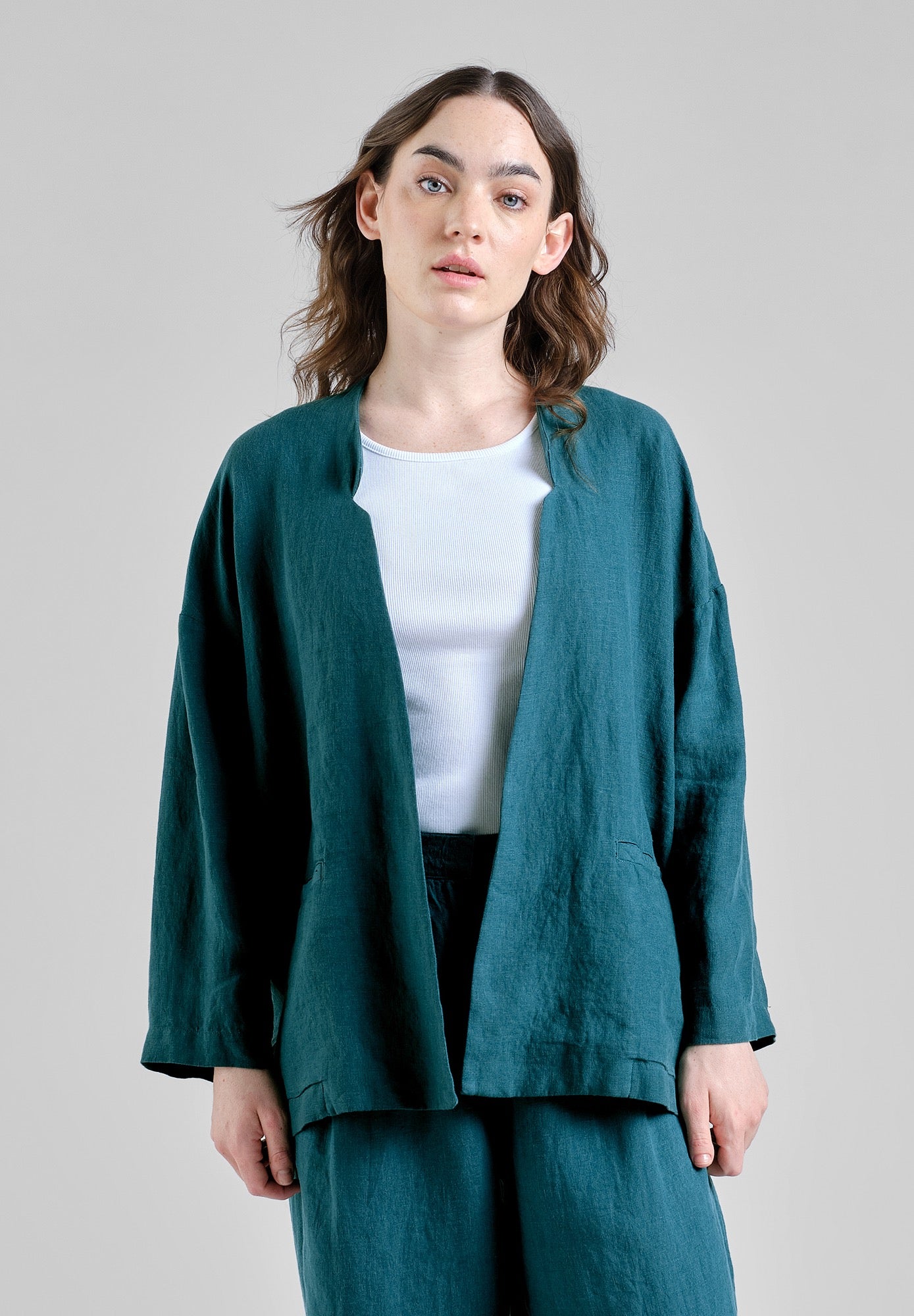Woman wearing a teal linen jacket and pants on a plain background
