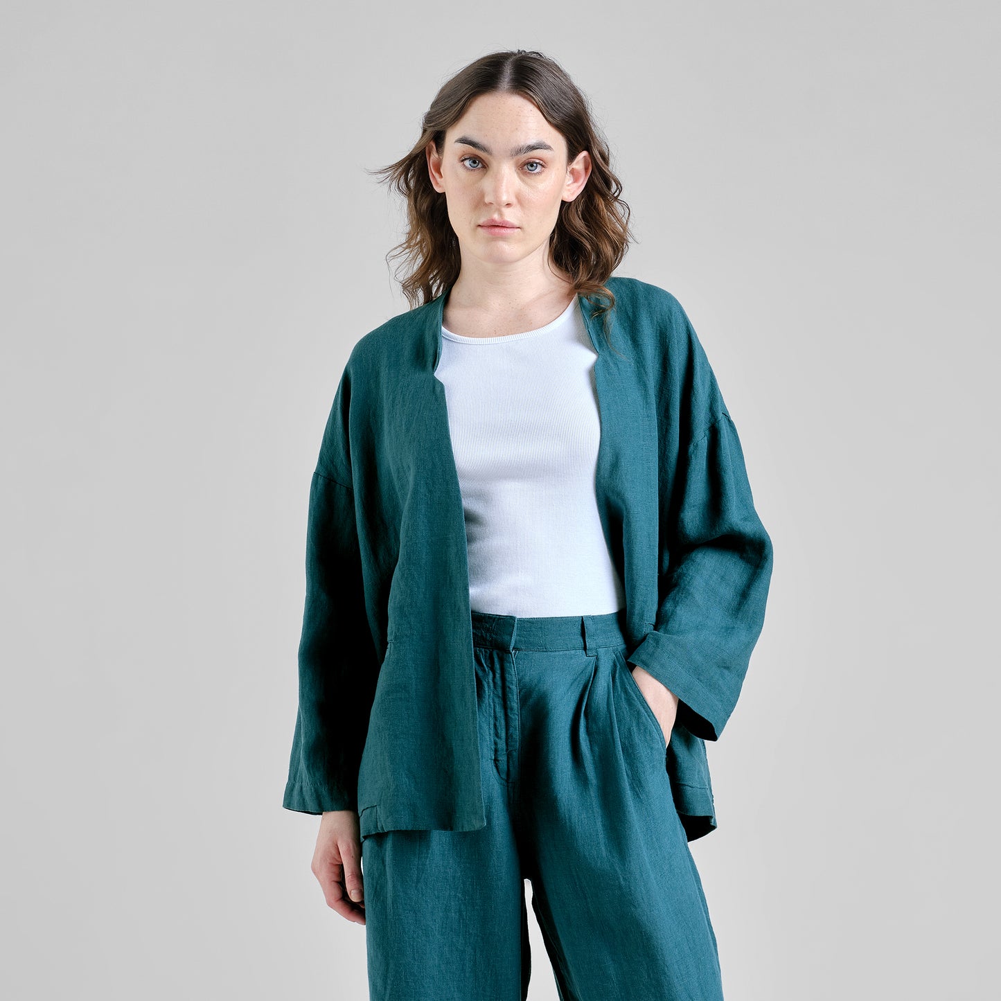 Woman wearing a teal linen outfit with a white top on a gray background