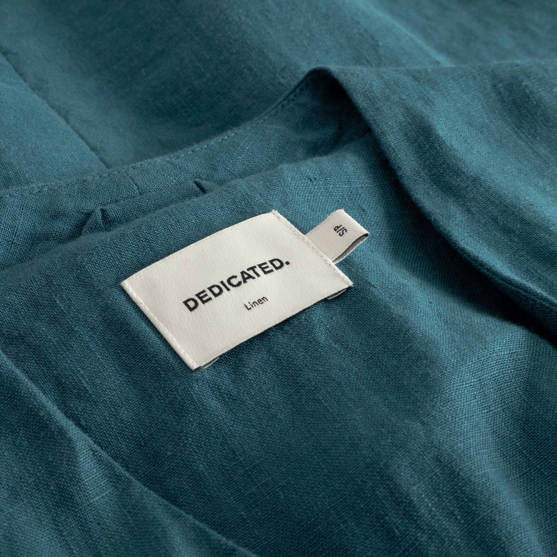 Teal linen fabric with a 'DEDICATED' label on a white background