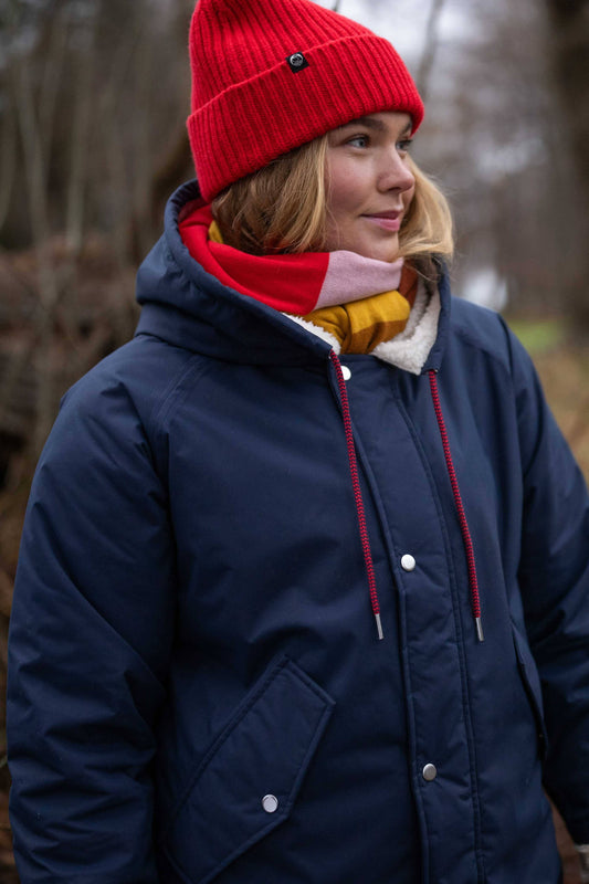 Woman wearing a red knit hat and the Danecoast waterproof winter parka in dark navyfrom Danefae Copenhagen in a forest setting