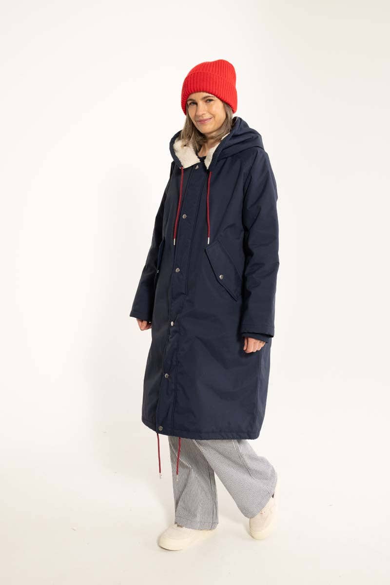 Woman wearing a long navy coat, tge Danecoast waterproof winter parka from Danefae, with a red beanie on a white background