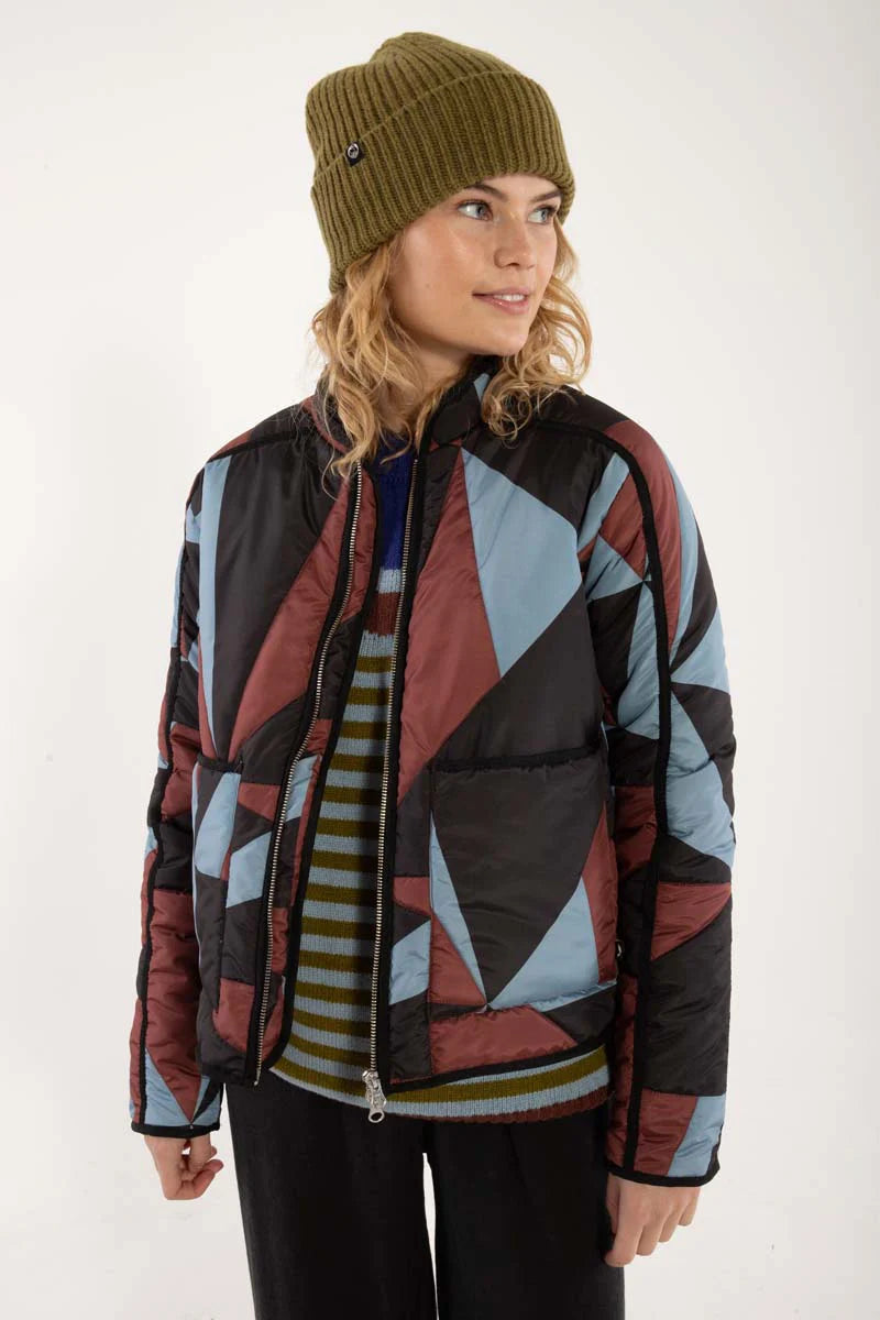 Woman wearing a thermal jacket from Danefae, featuring a geometric pattern in ice blue, wine red and black, and green beanie on a white background