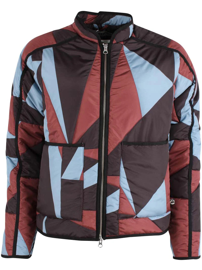 Woman wearing a thermal jacket from Danefae, featuring a geometric pattern in ice blue, wine red and black, and green beanie on a white background