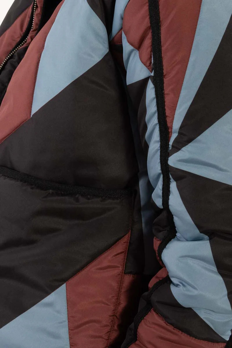 Woman wearing a thermal jacket from Danefae, featuring a geometric pattern in ice blue, wine red and black, and green beanie on a white background