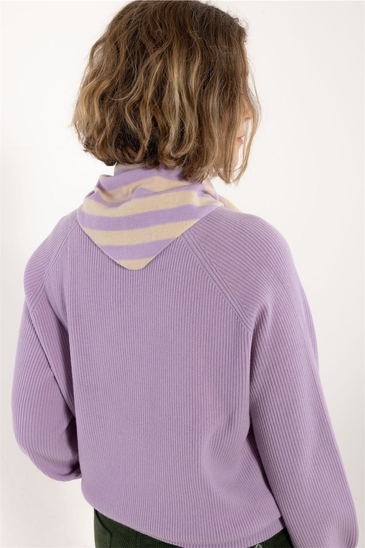 A woman shown from the back wearing a lavender ribbed knit sweater with a triangle scarf by Danefae featuring beige and lavender horizontal stripes, against a plain off-white background.