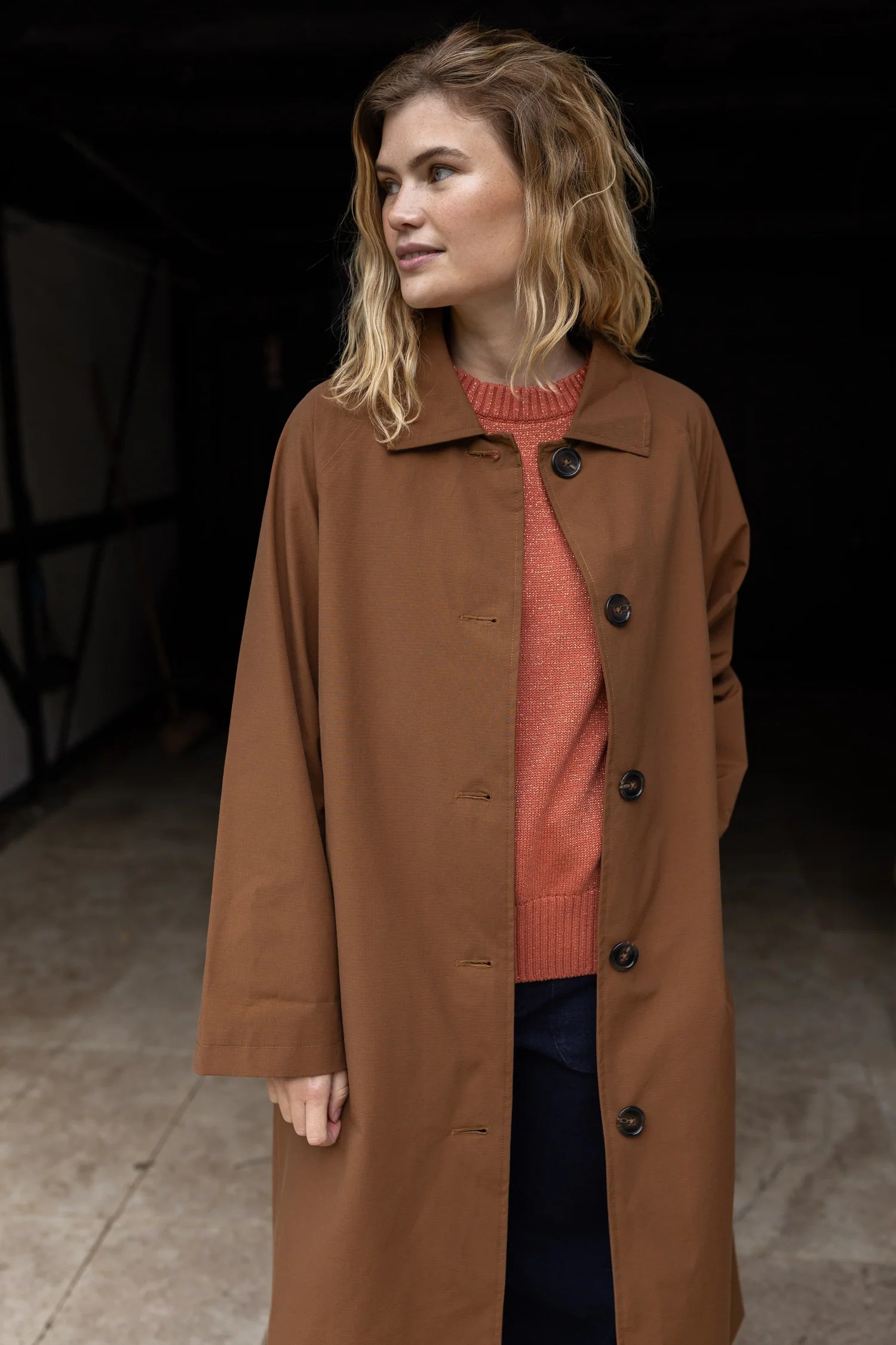 Woman wearing a brown coat over a red sweater against a dark background