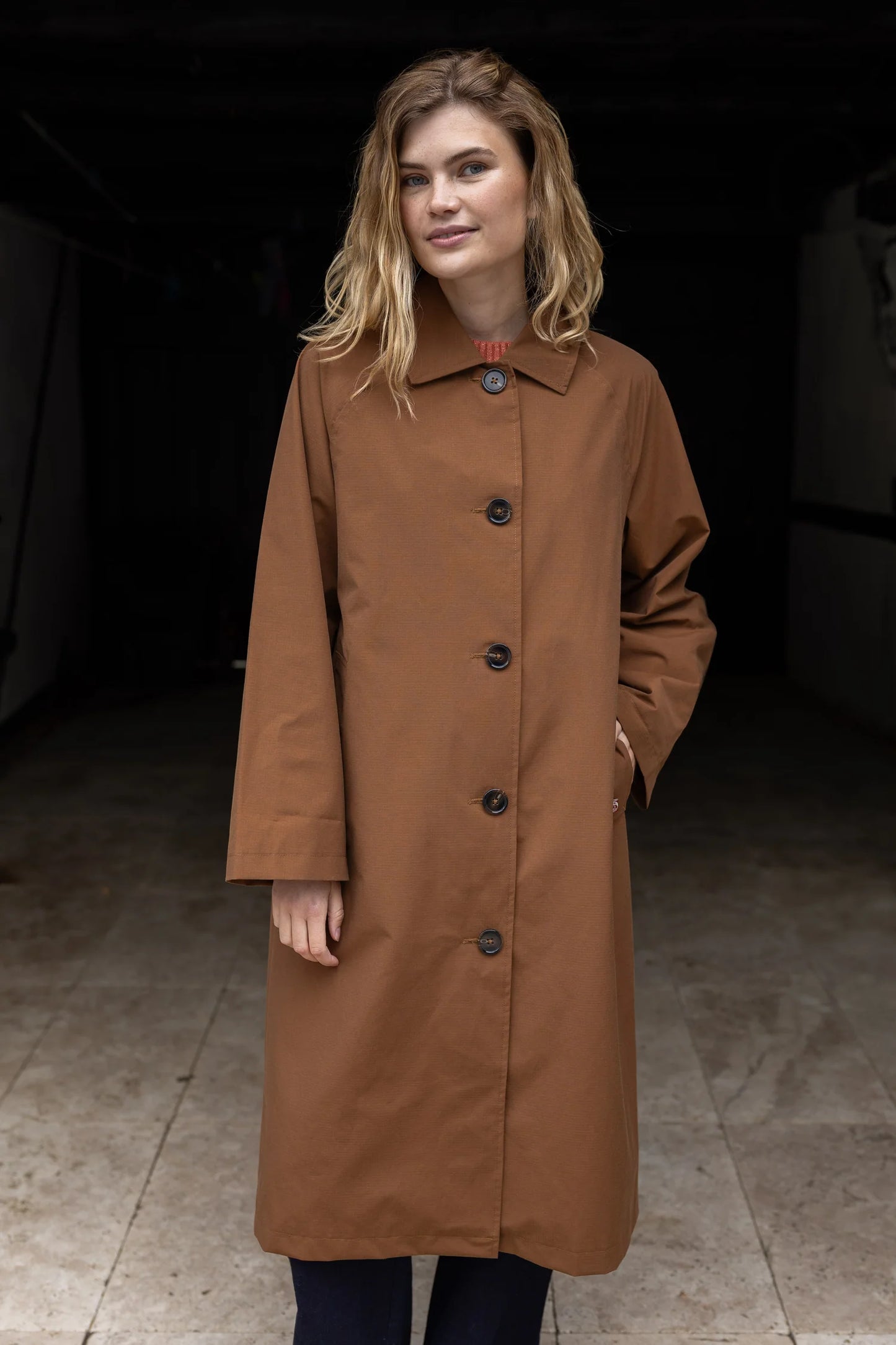 Woman wearing a brown coat standing in a dark indoor setting