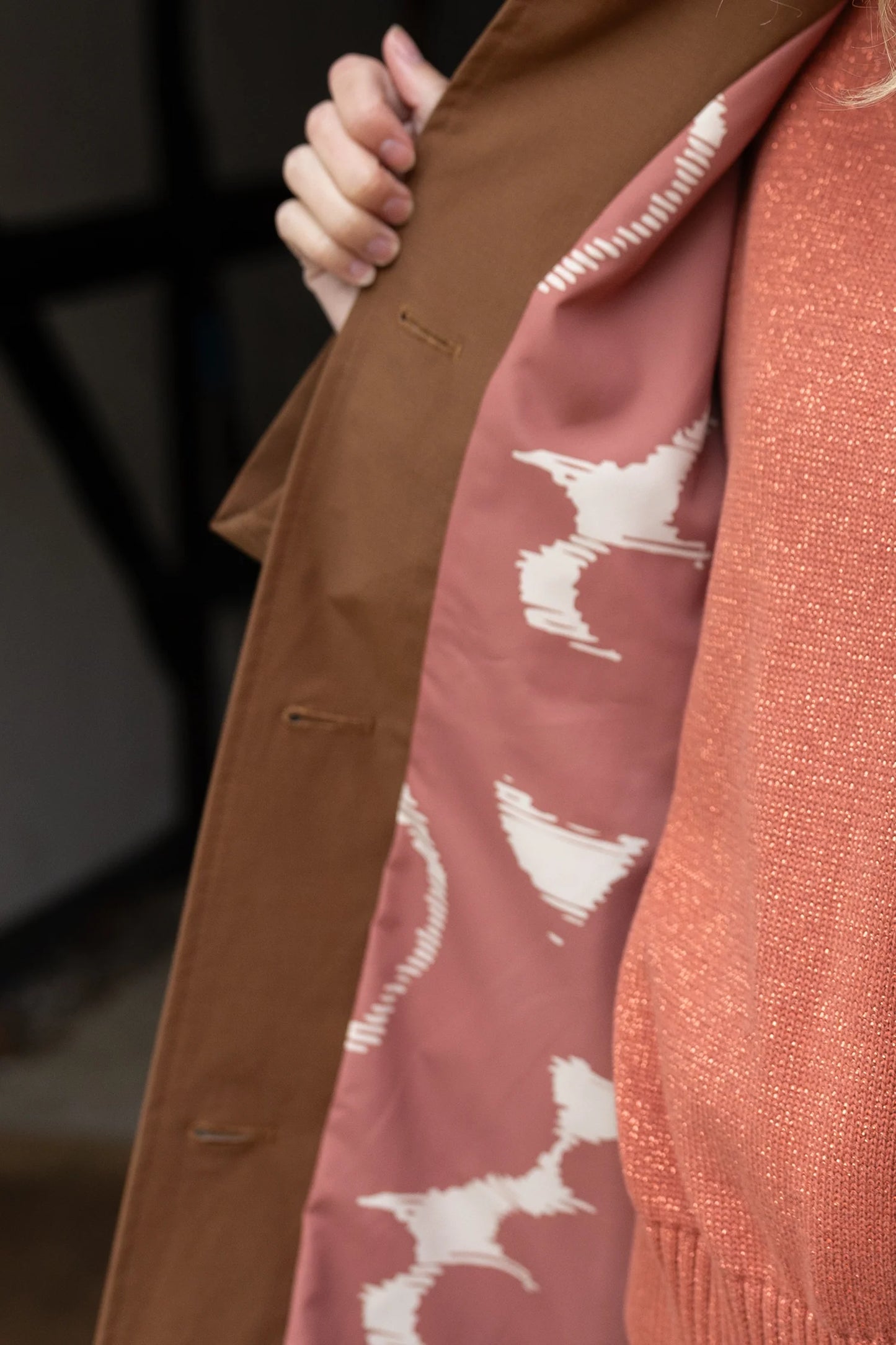 Close-up of a person wearing a brown coat over a pink garment with white patterns.