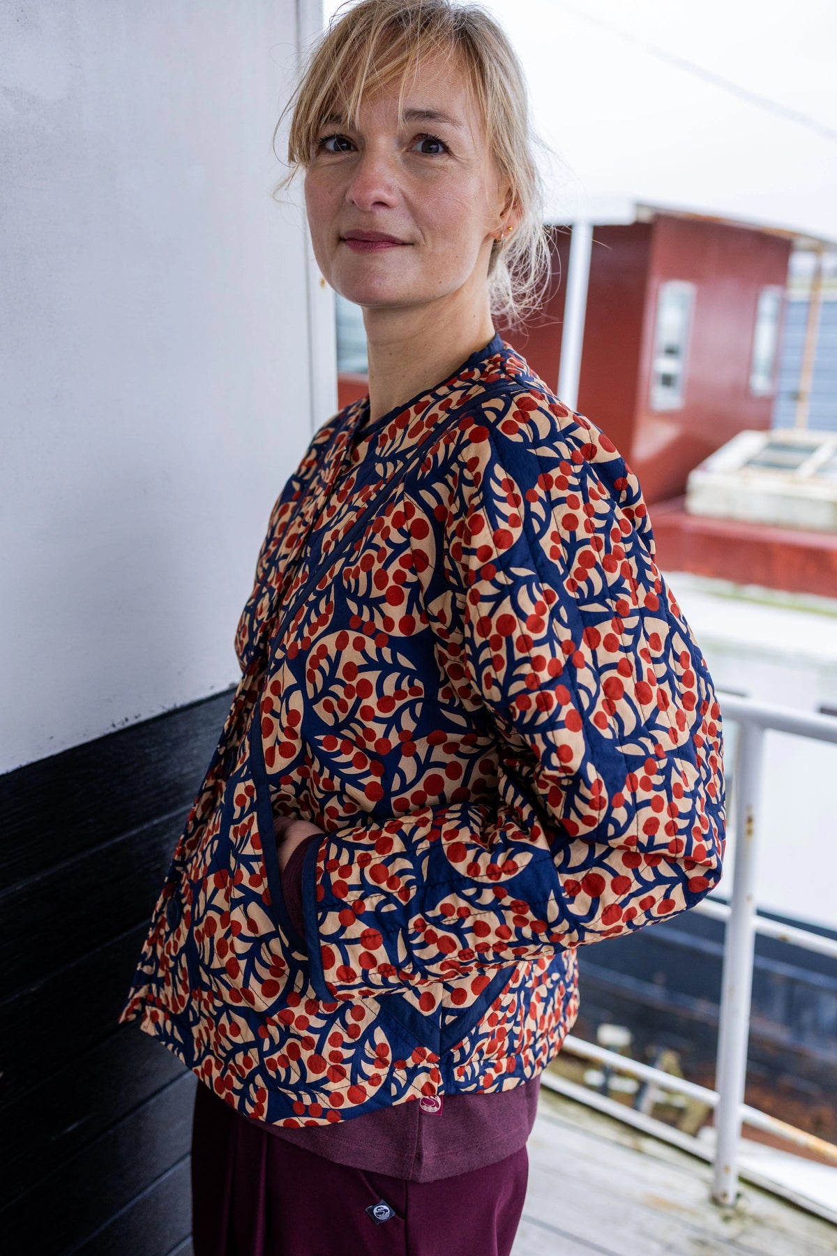 Woman wearing a patterned  quilted jacket by Danefae standing on a balcony