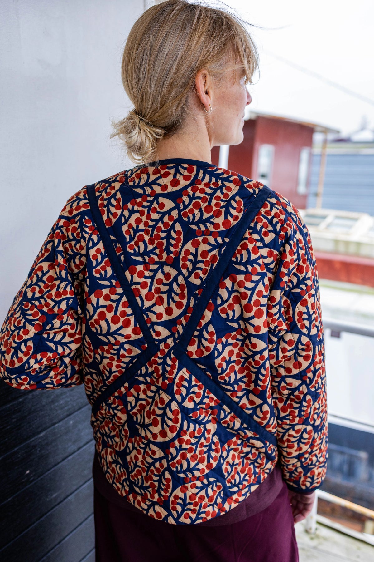 Person wearing a patterned sweater standing on a balcony with a building in the background