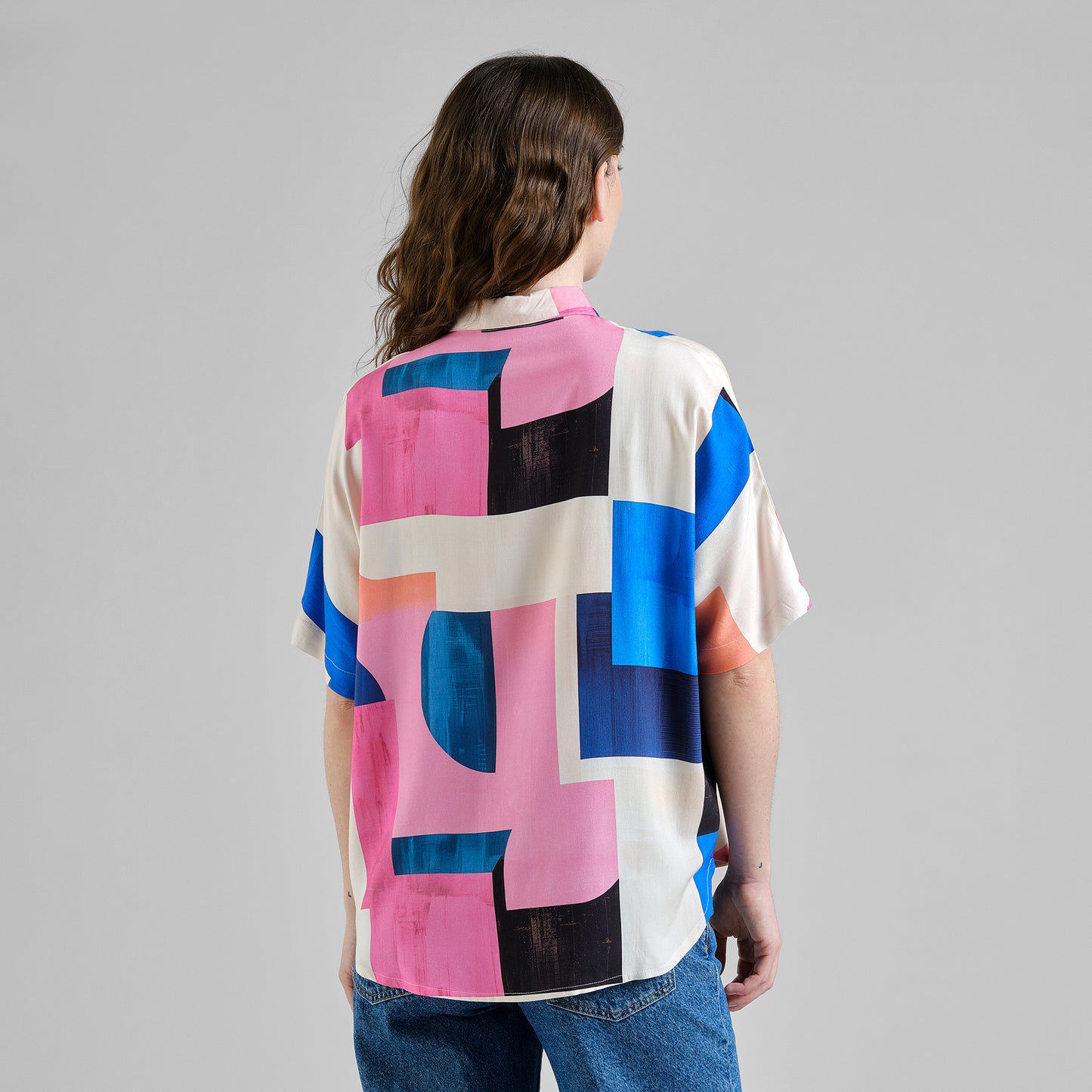 Person wearing a colorful geometric patterned shirt on a gray background