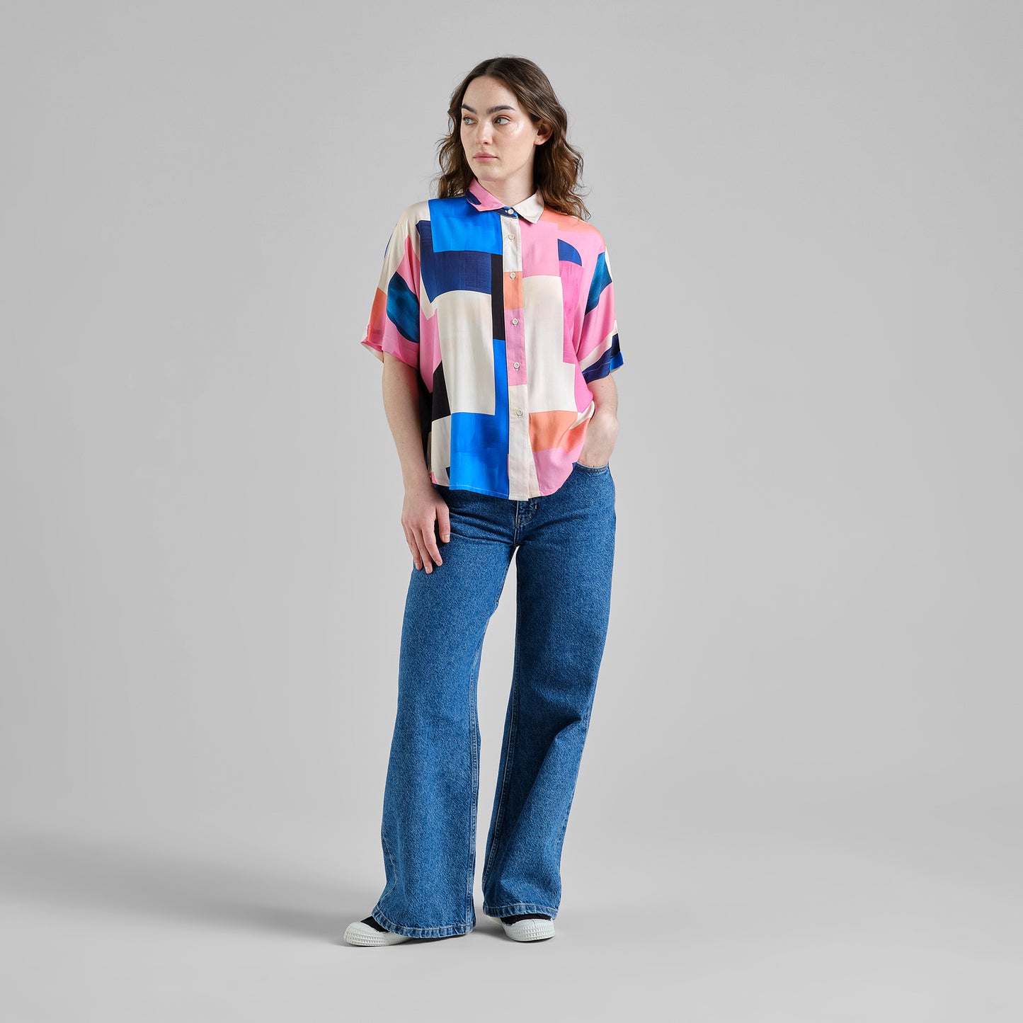 Person wearing a colorful geometric-patterned shirt and blue jeans on a gray background
