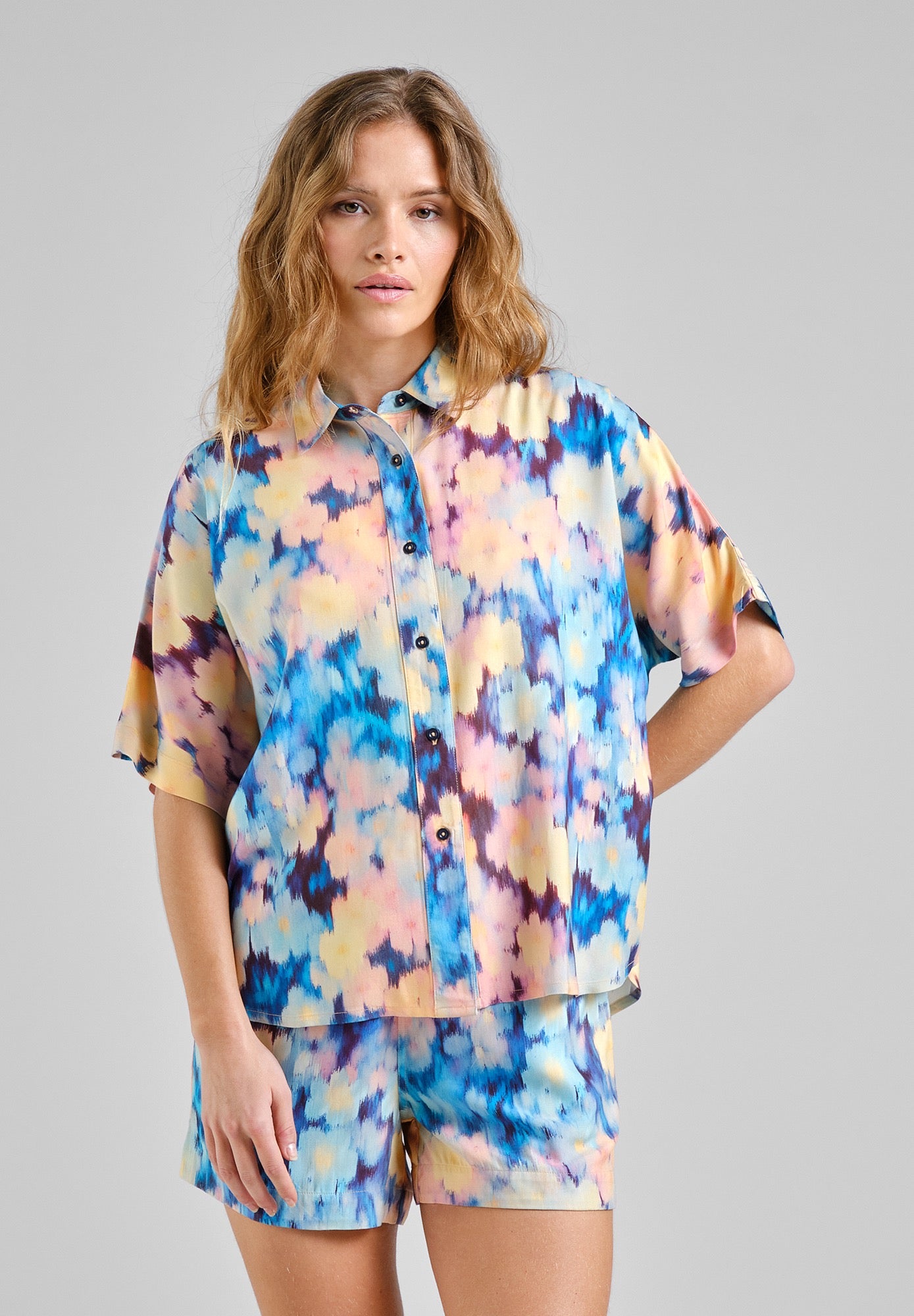 Woman wearing a colorful shirt and shorts set on a gray background