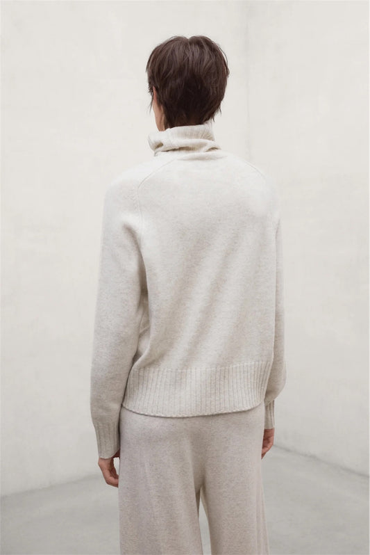 A woma shown from the back wearing a light cream wool knit turtleneck jumper from Ecoalf and matching knit pants in a minimalist studio setting.