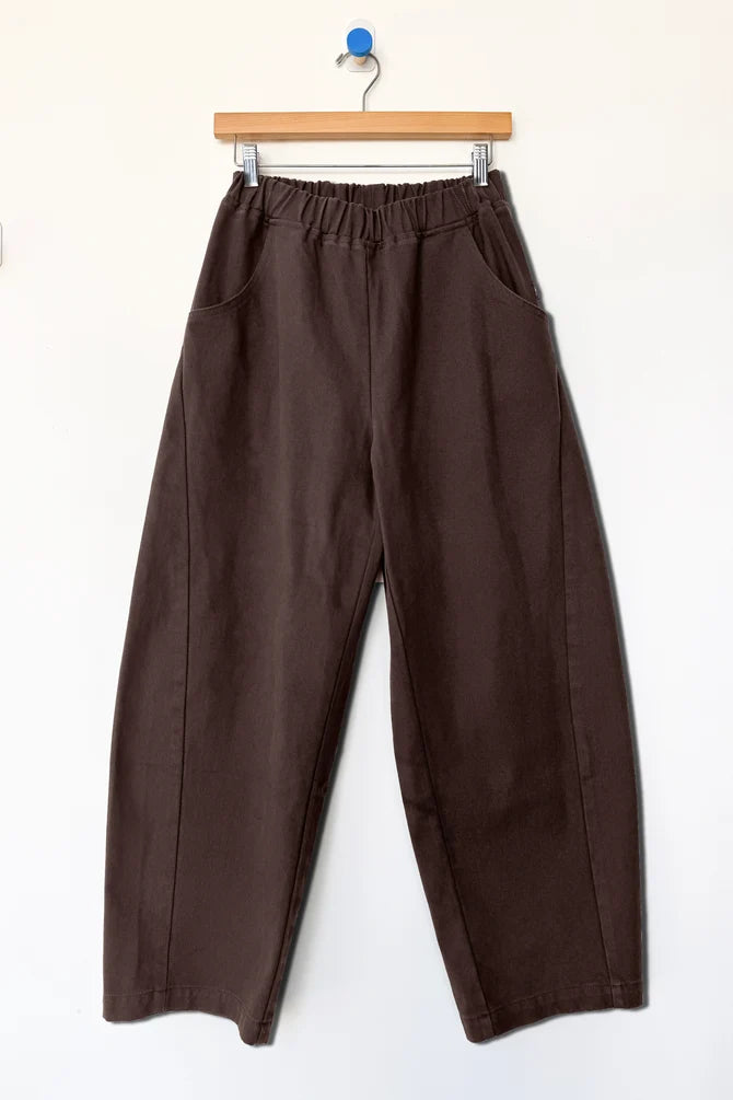  pair of wide-leg cropped Arc pants by Le Bon Shoppe in a dark chocolate brown color, hanging from a wooden hanger against a plain white wall.