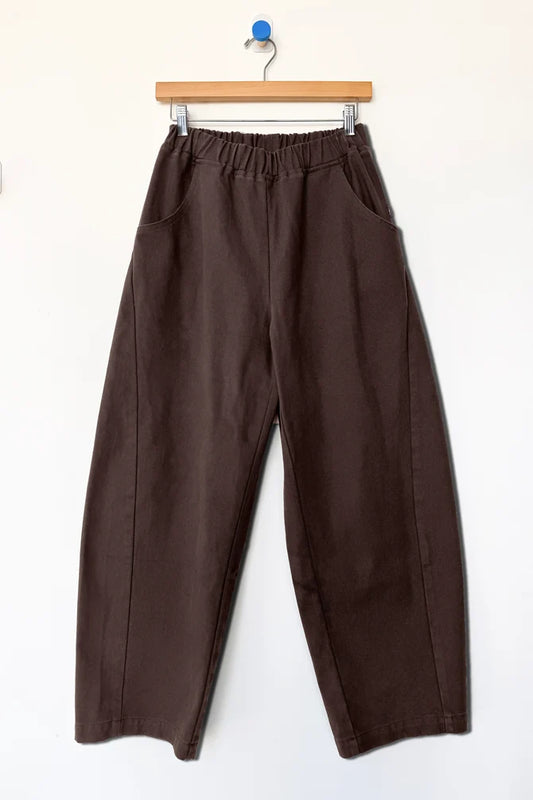  pair of wide-leg cropped Arc pants by Le Bon Shoppe in a dark chocolate brown color, hanging from a wooden hanger against a plain white wall.