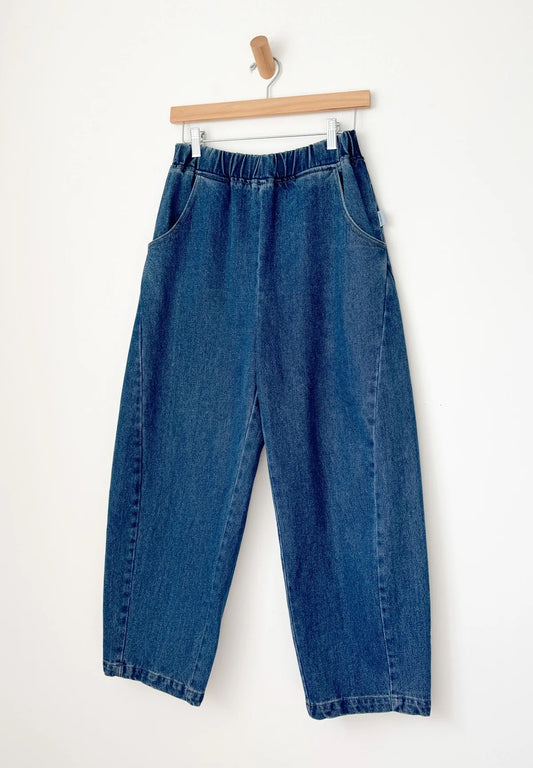 Arc Pants from Le Bon Shoppe. Barrel leg jeans made from durable 100% cotton denim. Featuring an elastic high waist, deep side pockets, and a slightly curved, cropped leg with a unique side panel. In a mid denim blue colour.