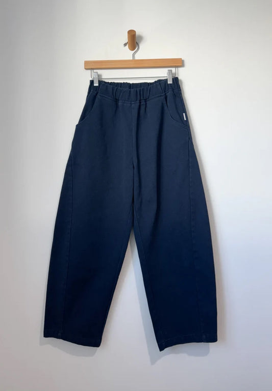 Arc Pants from Le Bon Shoppe. Barrel leg trousers made from durable cotton canvas. Featuring an elastic high waist, deep side pockets, and a slightly curved, cropped leg with a unique side panel. In a dark navy colour.