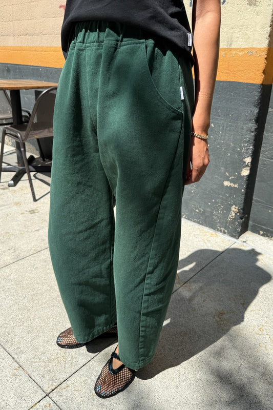 Arc Pants from Le Bon Shoppe. Barrel leg trousers made from durable cotton canvas. Featuring an elastic high waist, deep side pockets, and a slightly curved, cropped leg with a unique side panel. In a deep pine green colour.