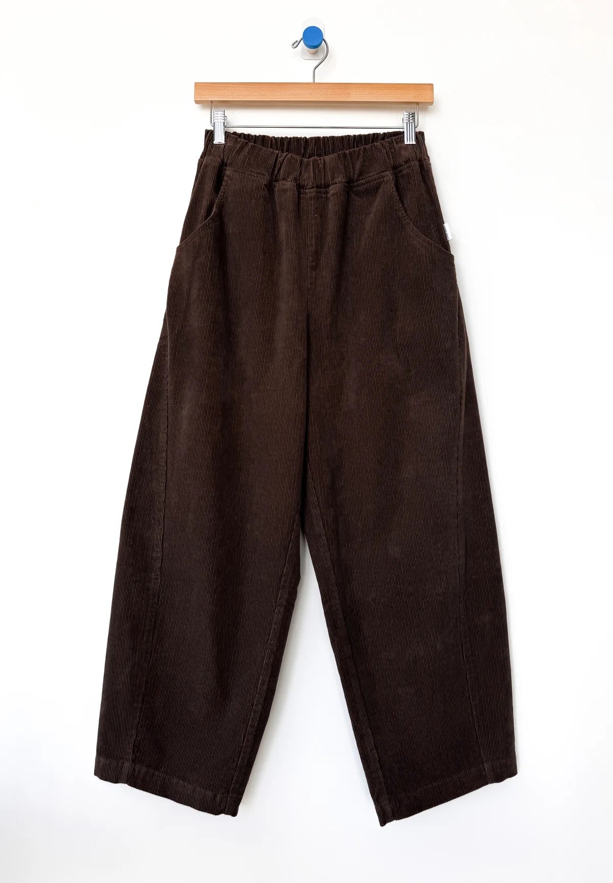 Brown barrel-leg corduroy Arc pants from Le Bon Shoppe hanging on a wooden hanger against a white background