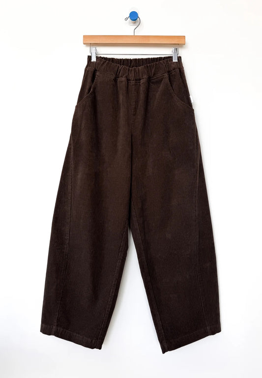 Brown barrel-leg corduroy Arc pants from Le Bon Shoppe hanging on a wooden hanger against a white background