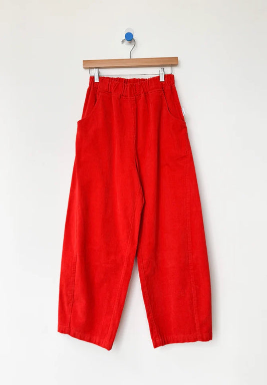 Bright red corduroy Arc pants from Le Bon Shoppe hanging on a wooden hanger against a white background